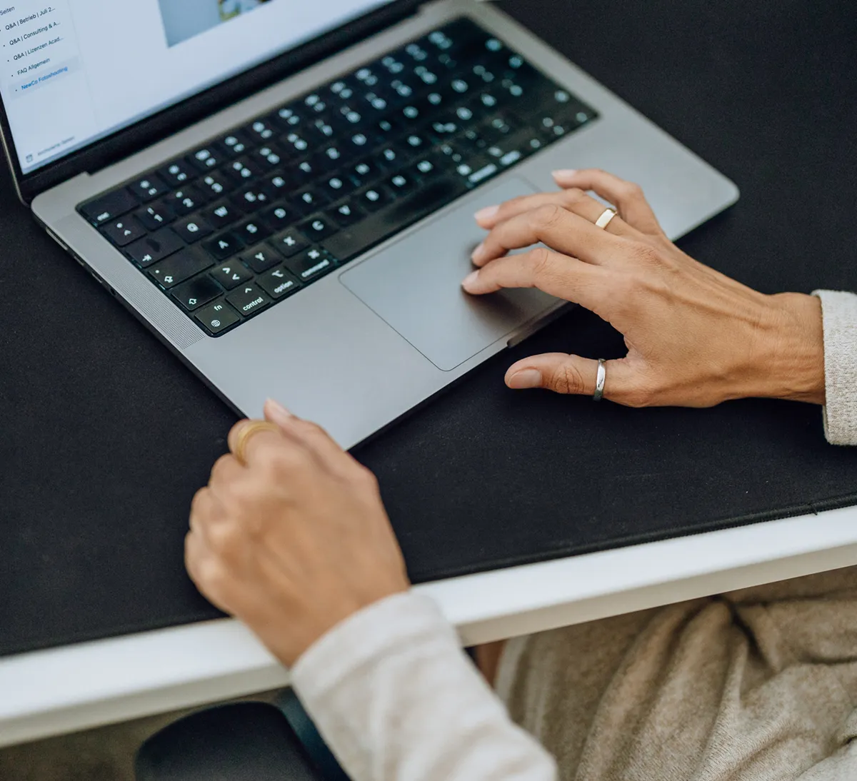 Close-up of hands typing on a laptop keyboard, with a focus on the touchpad and screen displaying a document.