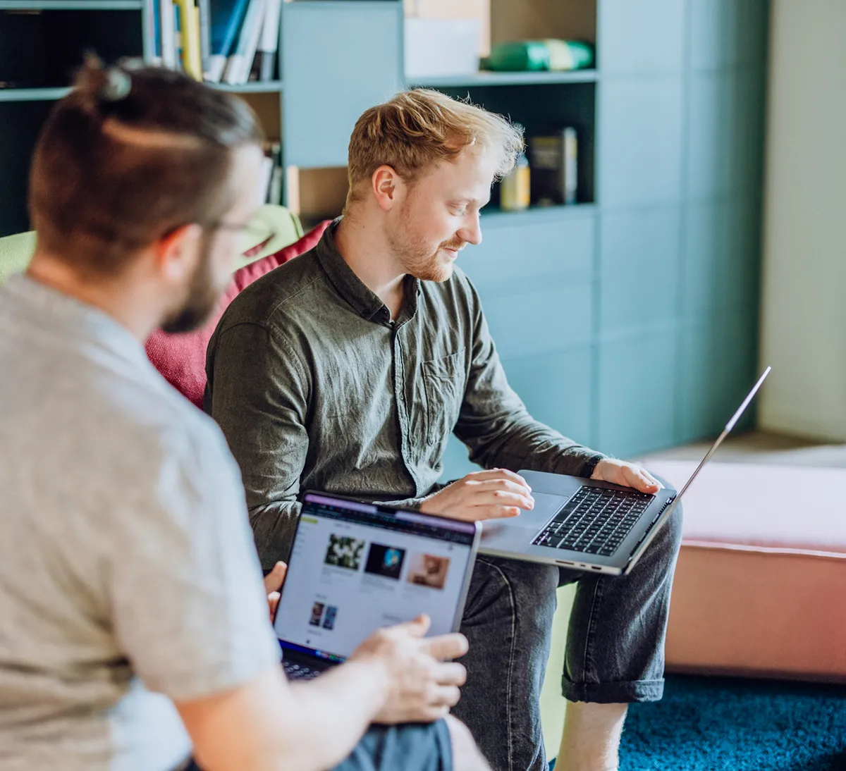 Two men sitting on colorful furniture, using laptops in a modern office setting.