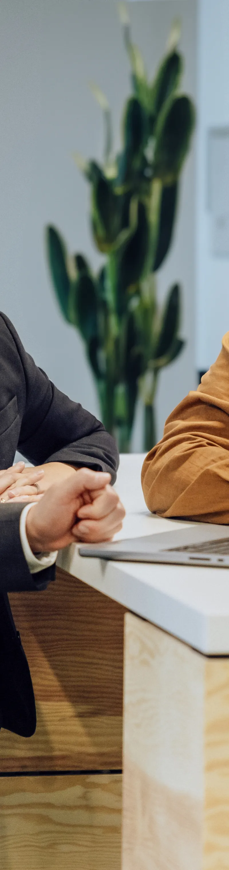 Three people in business attire having a discussion around a laptop on a wooden counter in an office setting.