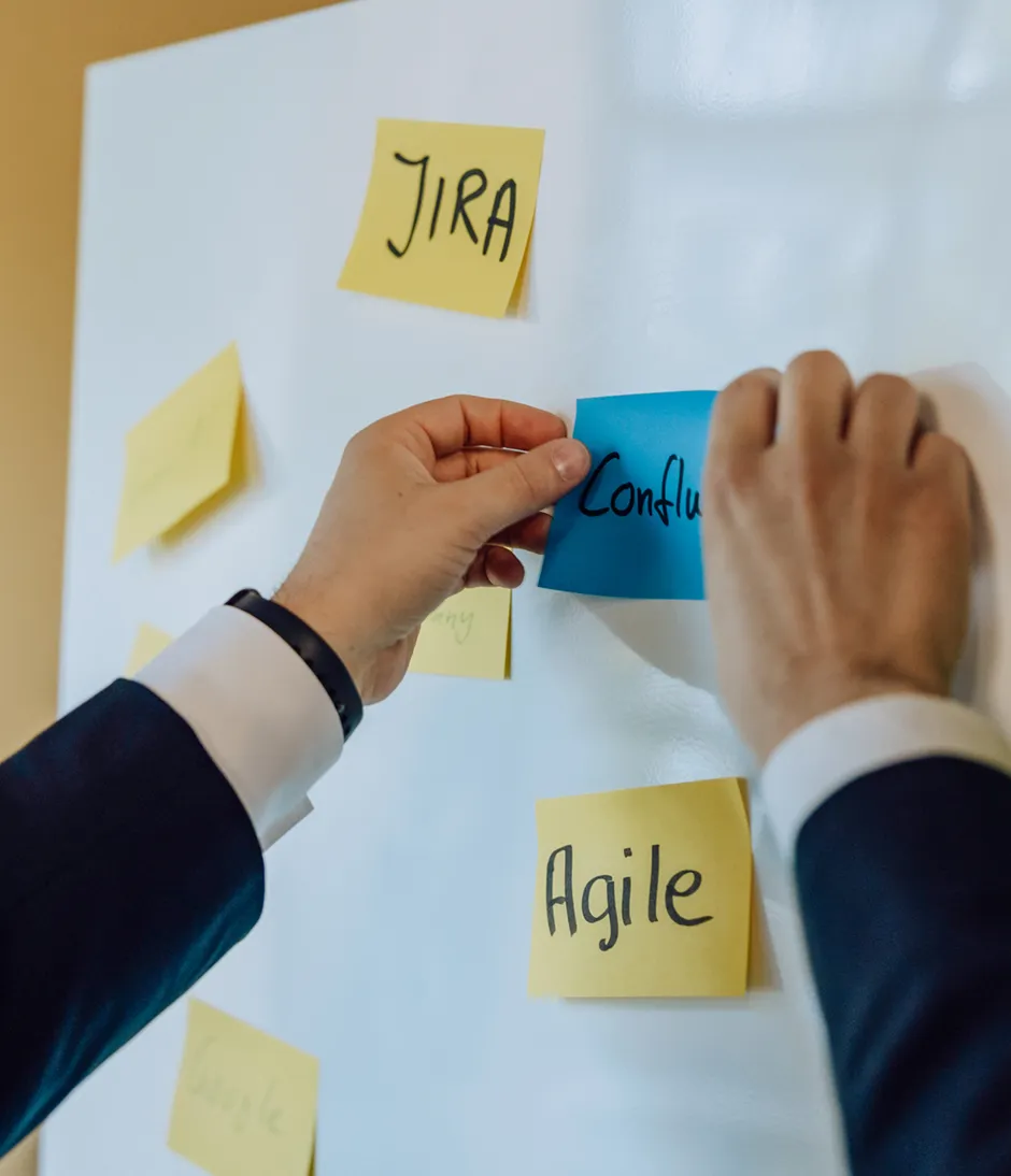 Person placing sticky notes on a whiteboard with words like JIRA and Agile.
